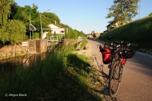 Fahrrad mit roten Packtaschen auf dem Kanalradweg. Sonne wirft lange Schatten.