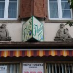 Zwei Sandsteinfiguren, dazwischen ein Schild mit der Aufschrift 'Fleurs'.
