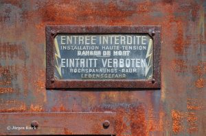 Verrostetes zweisprachiges Emaille-Verbotenschild an einer Trafostation.