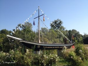 Schlankes, schwarzes Schiff mit Mast und Fähnchen, aufgestellt im Grünen als Dekoration
