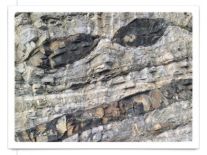 Screenshot einer Postkarte zeigt eine Felswand mit zwei unheimlichen schwarzen Augen, die sich offenbar als Magmaströme in den Gesteinsschichten ausprägten.