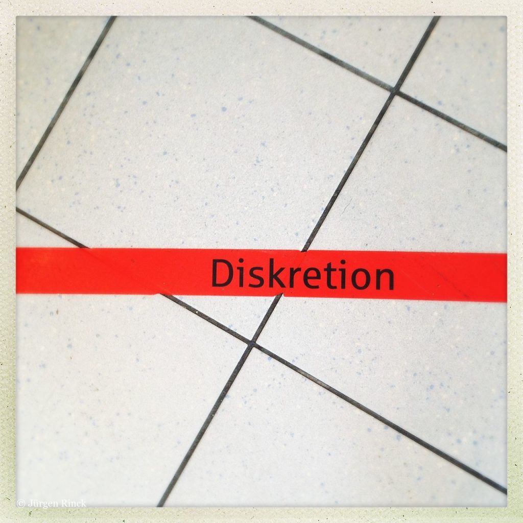 Das Wort Diskretion auf einem roten Streifen, der schräg über weiße Bodenfließen verläuft.