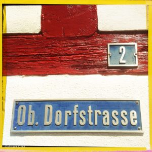 Haus Nummer zwei an rotem Fachwerkbalken. Darunter ein Schild Ob. Dorfstraße.