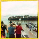 Drei Männer mit dem Rücken zum Betrachter fotografieren ein Containerschiff von der Aussichtsplattform eines Elbfährschiffs.
