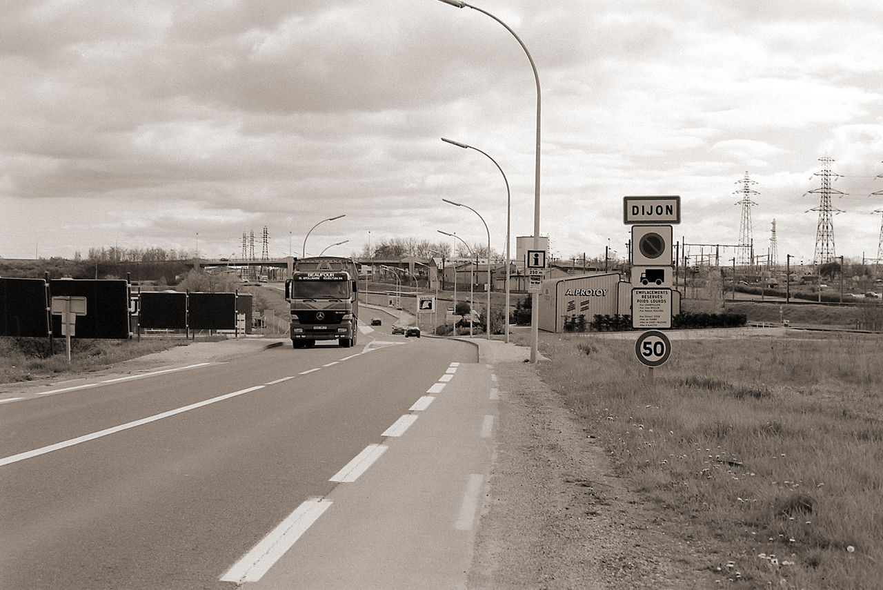 Straßenfoto vom rechten Straßenrand. Verkehrsreich mit entgegenkommendem LKW neben dem Ortsschild von Dijon.