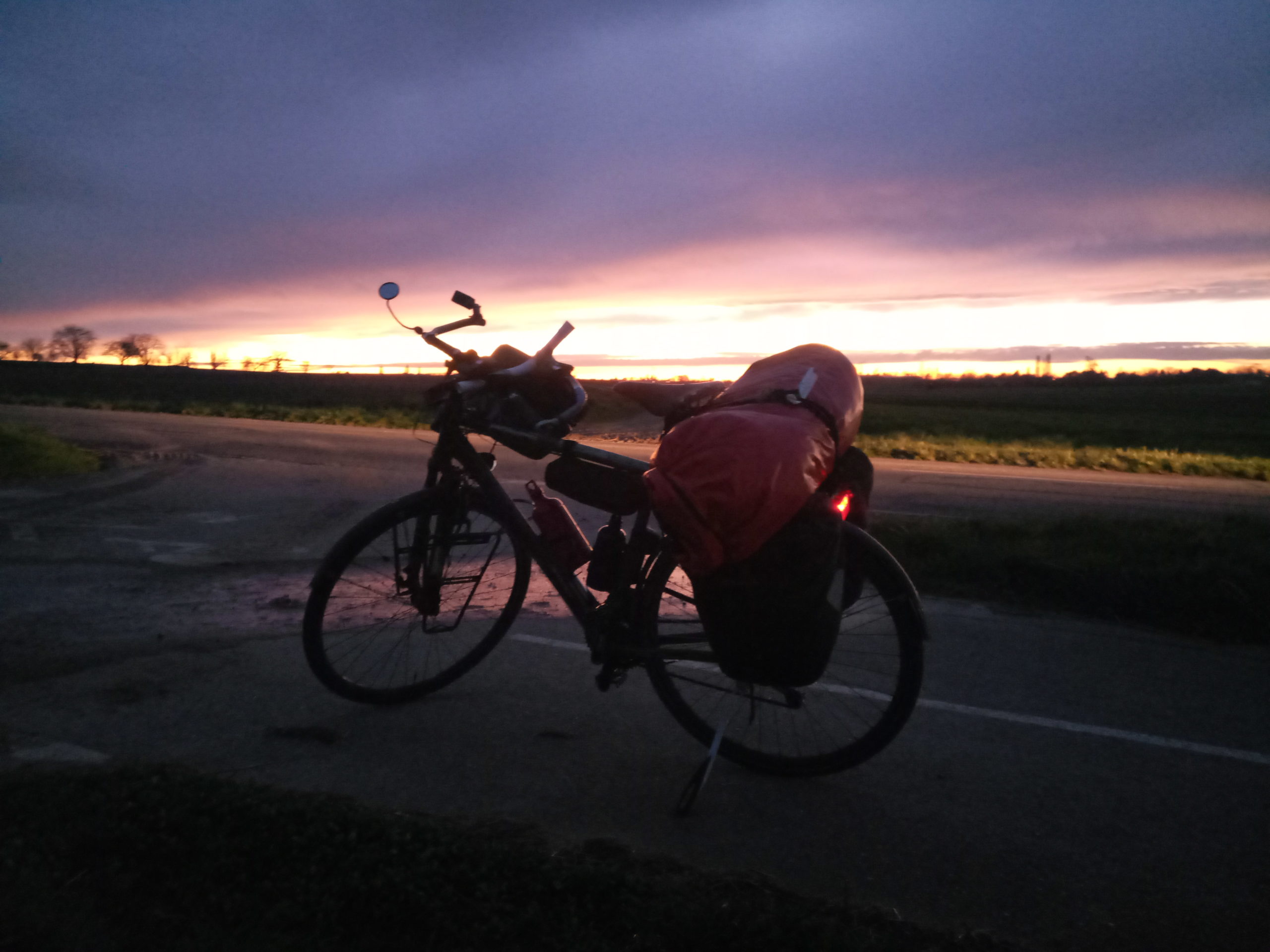 Reiserad fast im Dunkel vor einem rötlich orangenen Streifen Abendrot.
