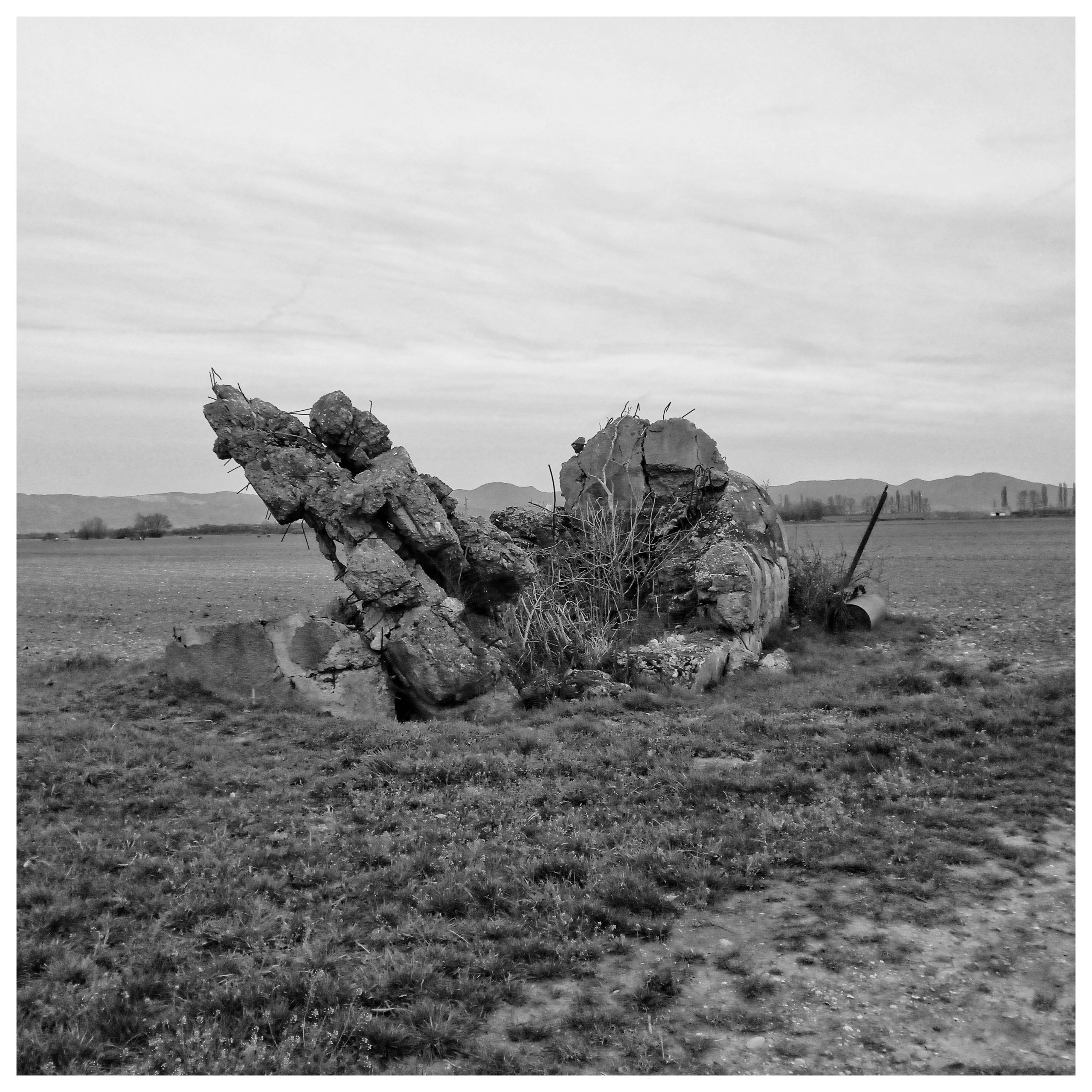 Die Reste eines Betonbunkers aus dem zweiten Weltkrieg ragen in diesem Schwarz-Weiß-Foto aus einer weiten, von Landwirtschaft geprägten Ebene
