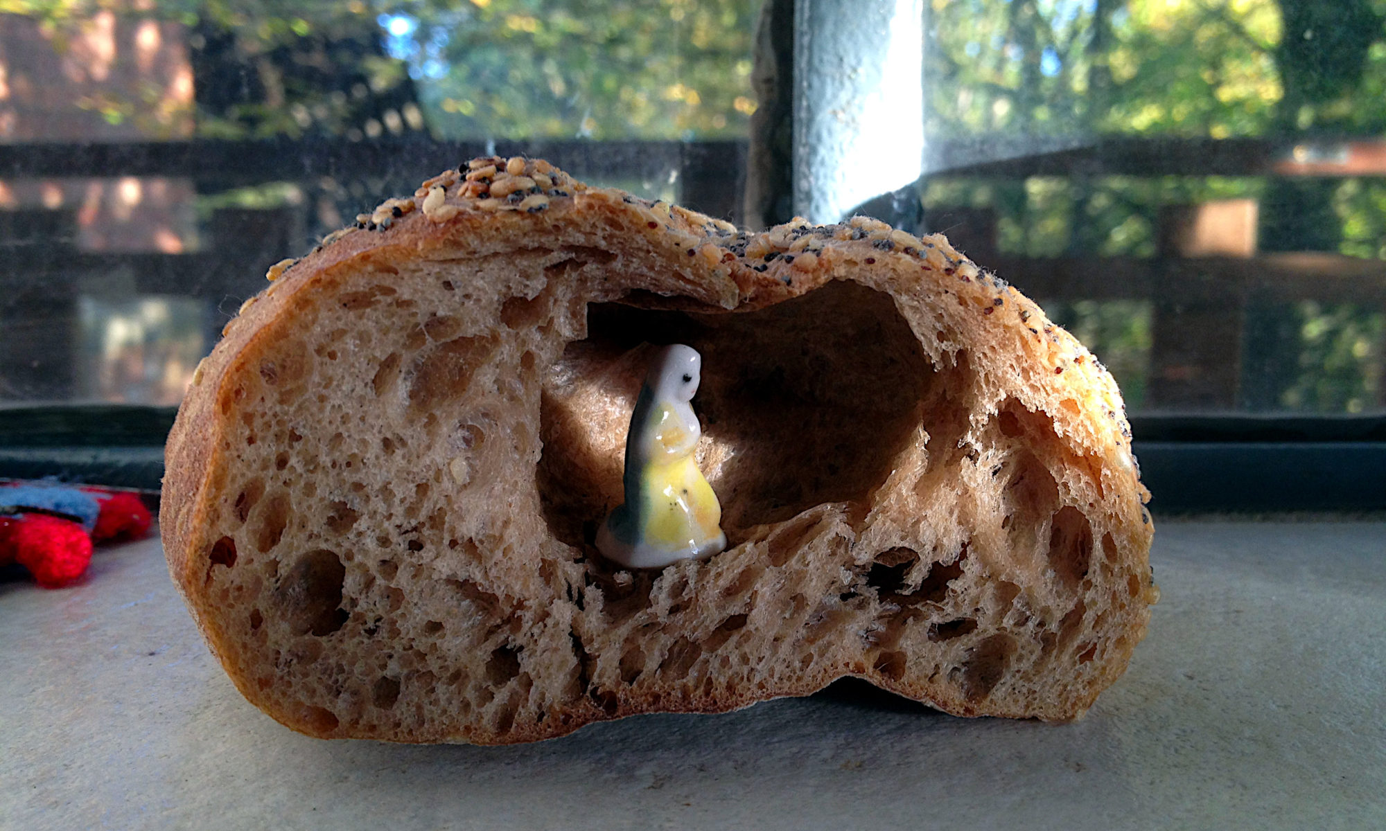Ein Kanten angeschnittenes Brot mit groben Poren und einem riesigen, natürlich gebackenen Loch, in dem eine Madonnenfigur aus Porzellan kniet.