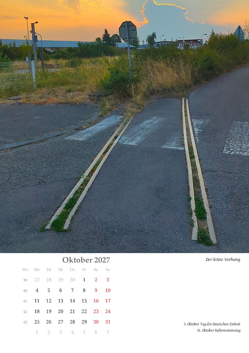 Eine Eisenbahnschiene endet abrupt im Teer der Straße. Über einen Zebrastreifen führt sie auf grüne Flächen hinzu, die sich vertrocknet vor einem düsteren Himmel mit gigantischer Turmwolke verlieren. Hinter der Wolke zeichnet sich ein Sonnenaufgang ab.