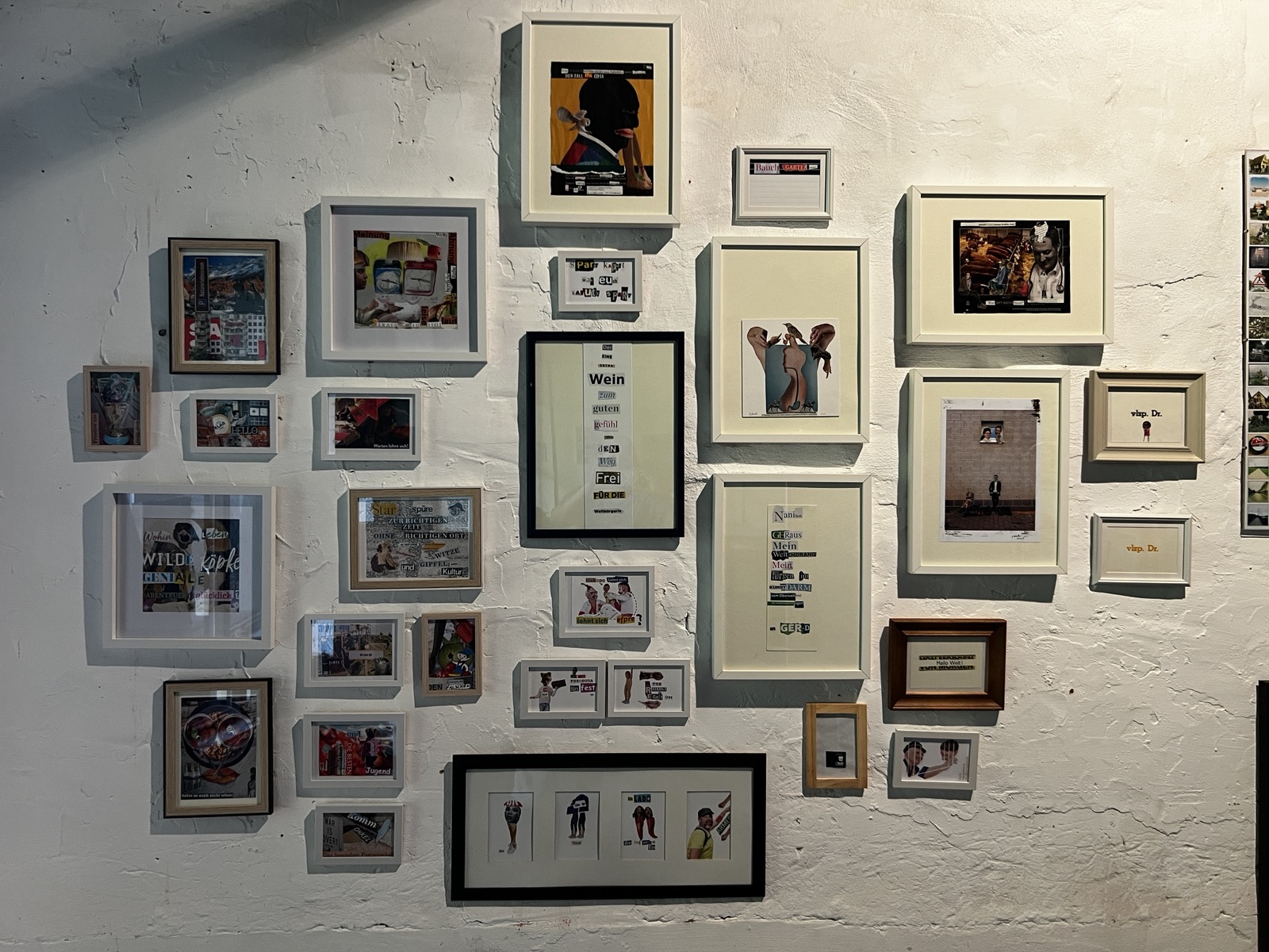 Eine komplexe Hängung von etwa 30 gerahmten, unterschidelich großen Collagenbildern an einer weißen Atelierwand